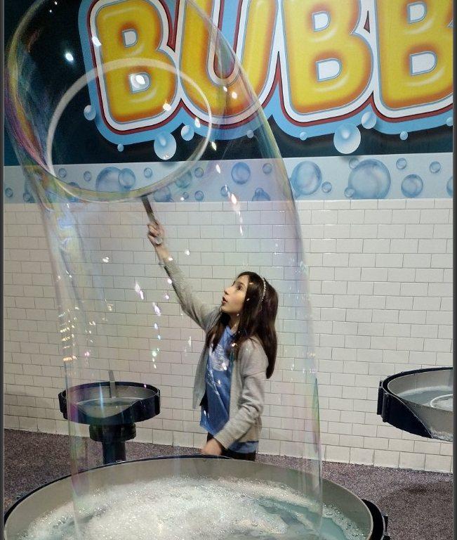 A student stretching a giant soap bubble on a science museum field trip
