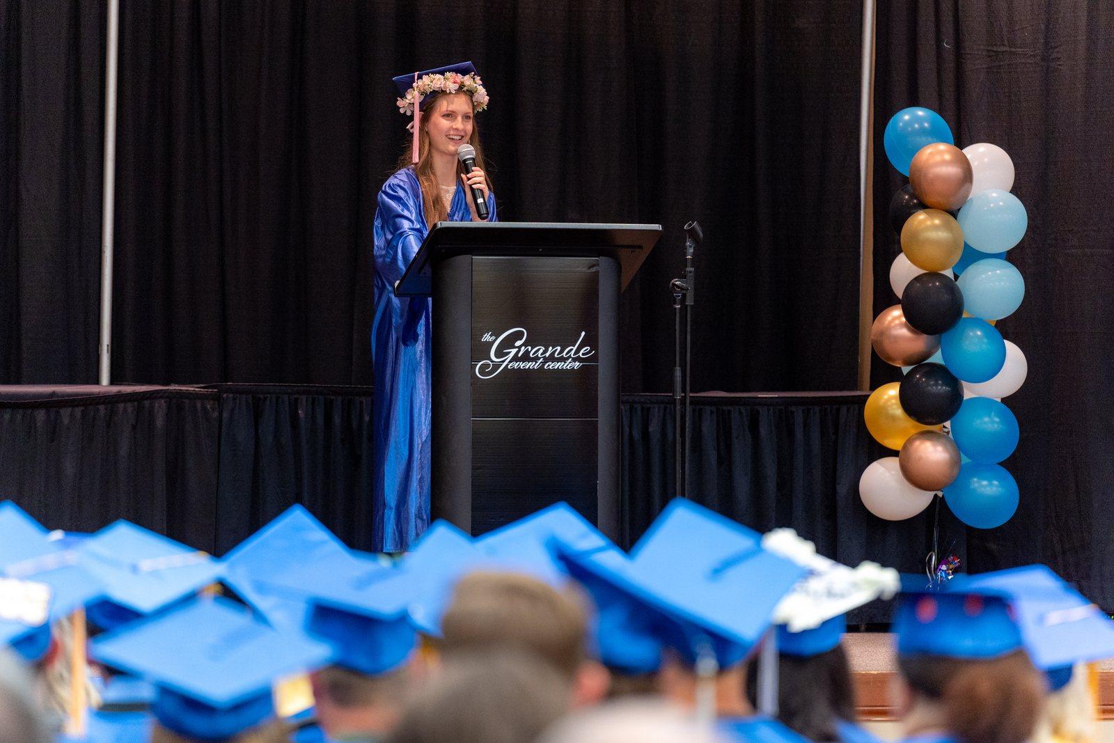 An AliYah Academy graduate in cap and gown speaking at the podium during the graduation ceremony