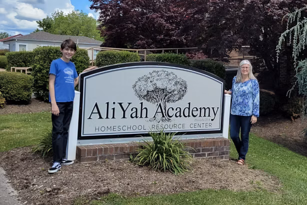 Katie and a student in front of the AliYah Academy Homeschool Resource Center sign in Morristown, Tennessee